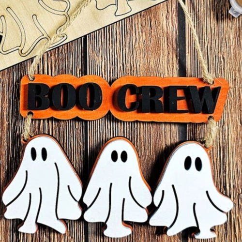 Halloween decoration with 'BOO CREW' sign and ghost shapes on a wooden background from Melissa Rae and Company